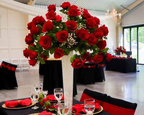 event management, event decoration, wedding rentals durham nc, wedding decorators near me wedding planners, wedding decoration, wedding rustic decor, wedding staging, wedding white arch, white balloon decor, wedding decoration near me, wedding head table decor, wedding red table setting, gold chargers, red cloth napkins, gold napkin ring, tall clear vase, tall vase with red roses, chair coverings, red sash, black chair covers, small candles, greenery, table,