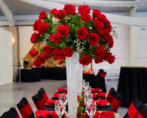 event management, event decoration, wedding rentals durham nc, wedding decorators near me wedding planners, wedding decoration, wedding rustic decor, wedding staging, wedding white arch, white balloon decor, wedding decoration near me, wedding head table decor, wedding red table setting, gold chargers, red cloth napkins, gold napkin ring, tall clear vase, tall vase with red roses, chair coverings, red sash, black chair covers, small candles, greenery, table,